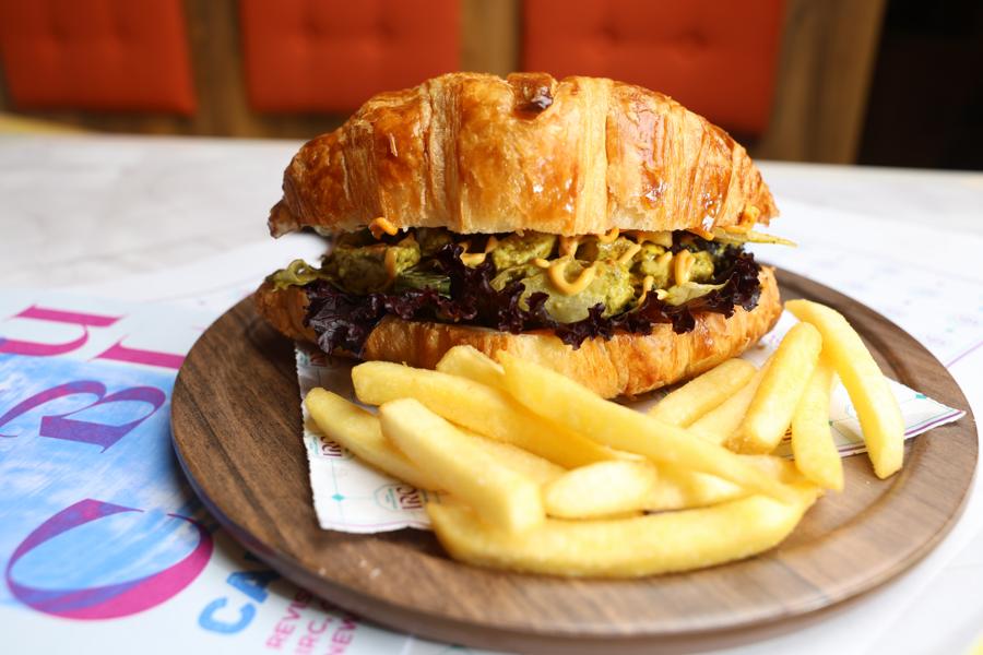 Croissant paneer tikka sandwich with fries on a wooden board