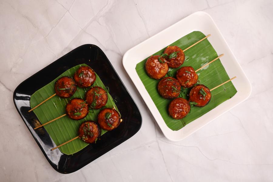 Glazed skewers on banana leaves on black and white plates