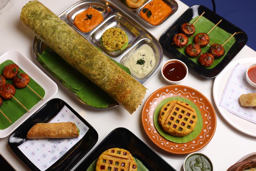 A table of dishes including pesto dosa, dosa onion rings and waffle bread pakora